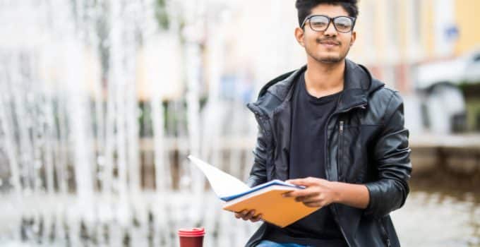 indian student man holding pile books sitting near fountain street 231208 2778