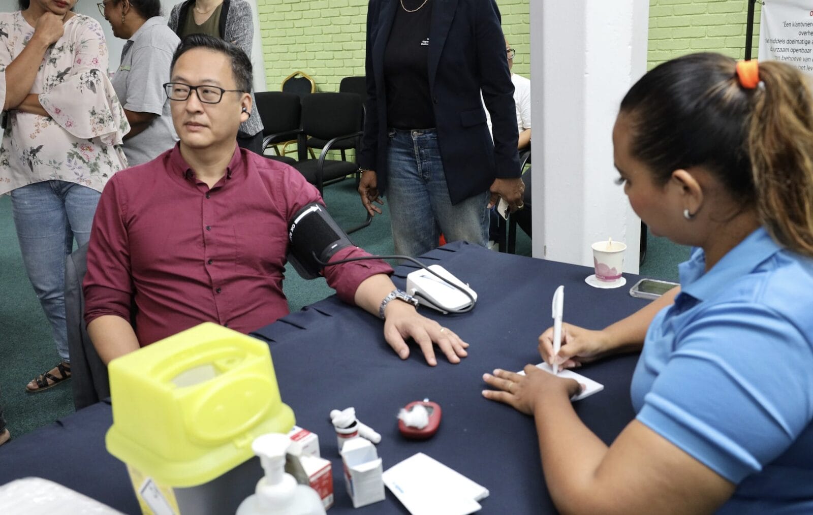 Medewerkers van OWRO (en minister Tsang) laten tijdens een gezondheidsscreening hun bloeddruk en bloedsuiker controleren. Foto: CDS